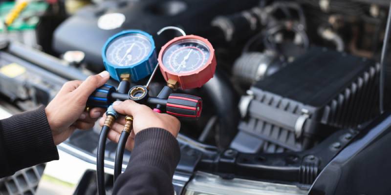 Technician using a dual-gauge manifold set to check a car's AC system under the hood.
