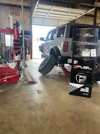 Gray SUV on a hydraulic lift inside a workshop, rear wheel raised, with stacked G FUEL boxes nearby.