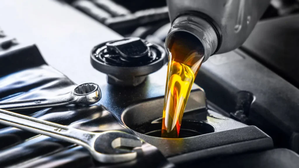 Close-up of engine oil being poured into a car's oil fill opening, with wrenches visible in the foreground.
