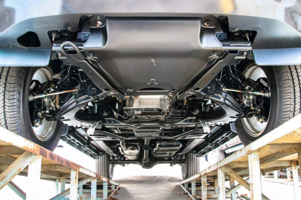 Underside of a car raised on a frame rack, showing suspension, exhaust, and drivetrain components from below = workshop view.
