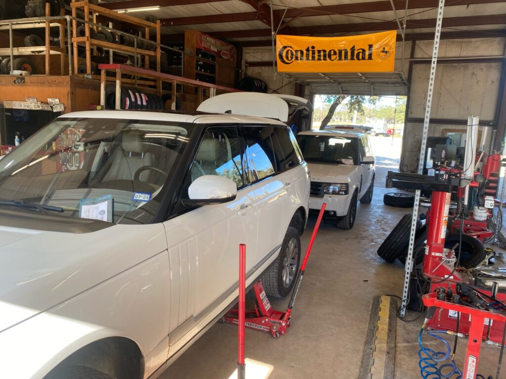 Auto repair shop interior with white SUVs on lifts, tire racks, and a yellow Continental banner overhead.