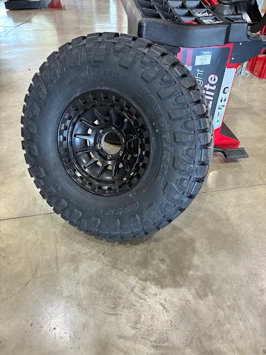 Large off-road tire mounted on a black alloy wheel, leaning against a red tool cart on a concrete shop floor