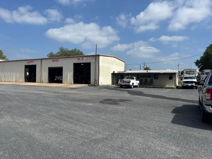 Auto repair shop with three open service bays on a sunny day; a white car parked outside.