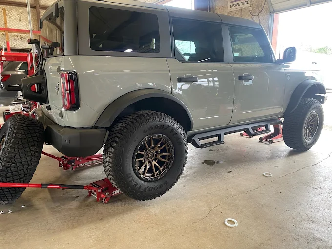 Lifted gray SUV on jack stands in a workshop, featuring oversized off-road tires and aftermarket wheels on a four-wheel drive.